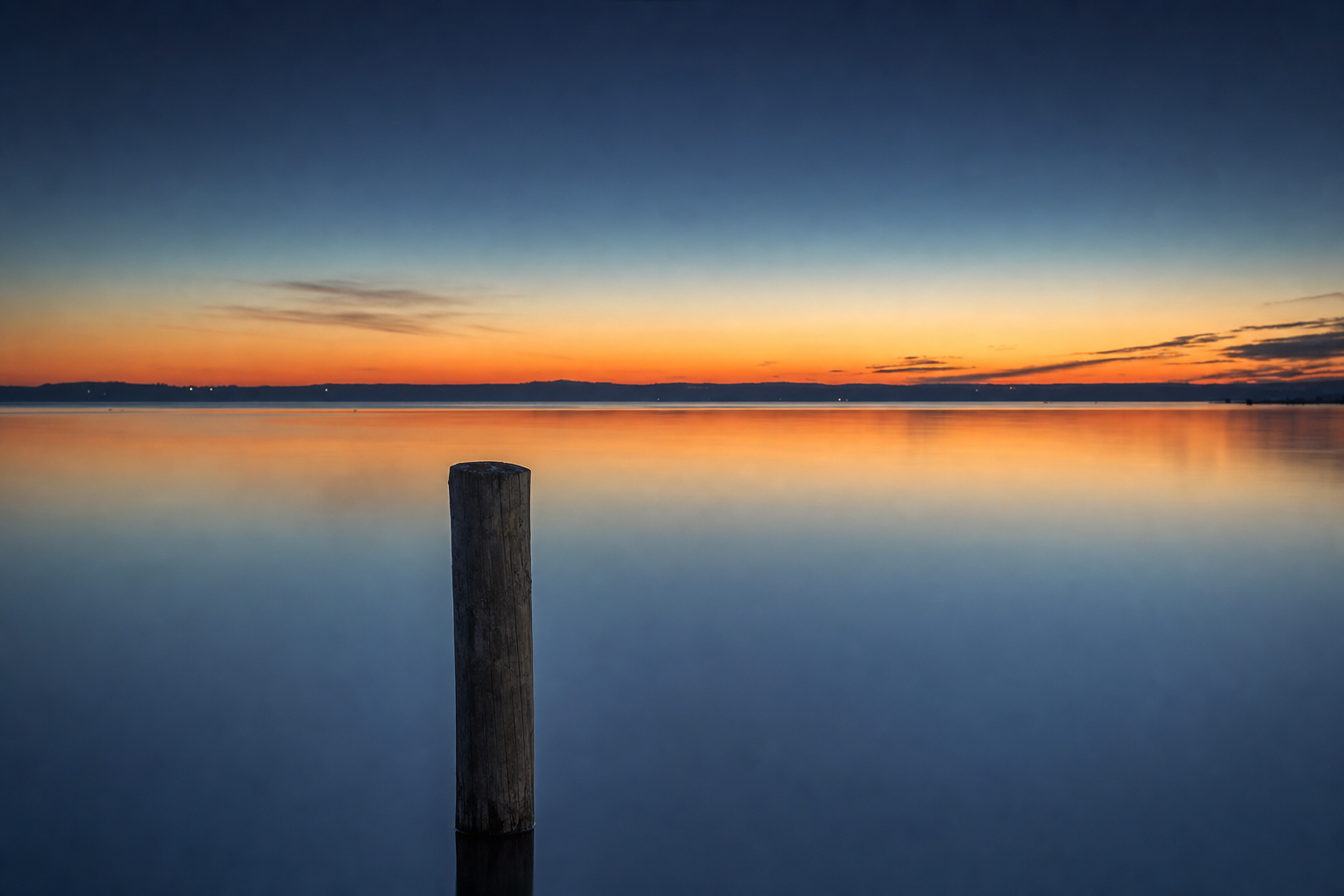A lone wooden pylon standing in the still, reflective water of Corio Bay at blue-hour dusk